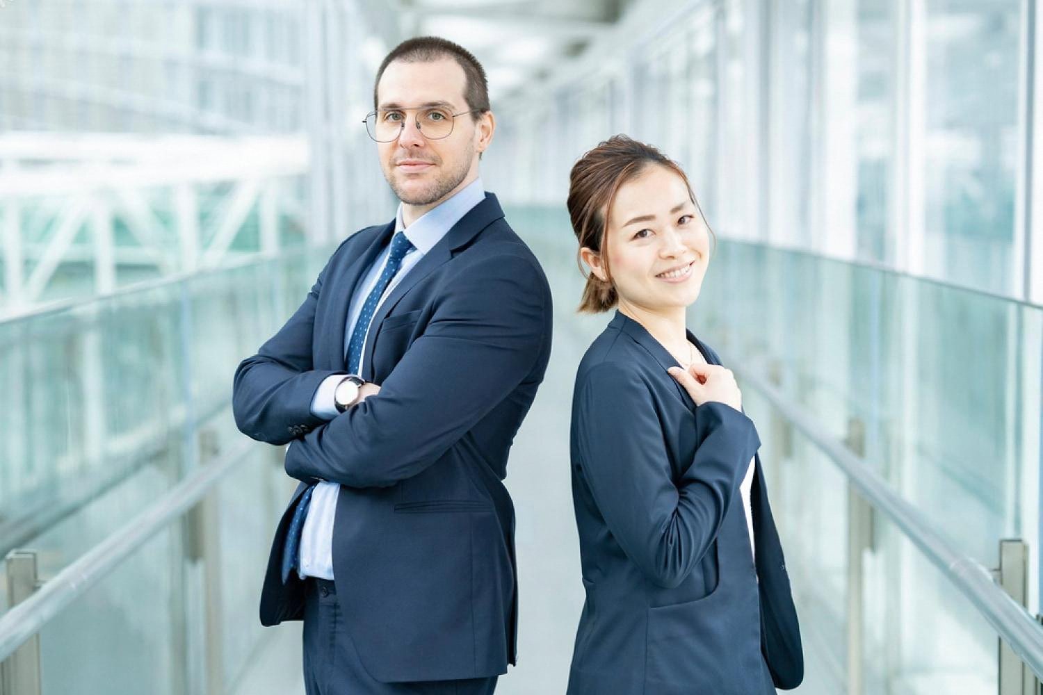 Two international colleagues standing back to back in a modern UAE office corridor